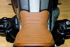 Selle en cuir marron vintage surpiquée pour moto custom avec réservoir gris et moteur noir.