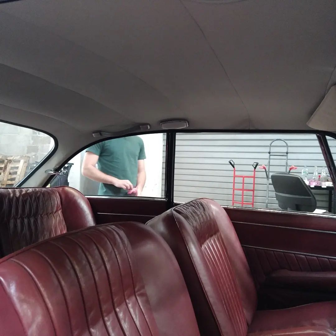 Intérieur de voiture vintage avec sièges en cuir rouge et homme en arrière-plan dans un garage de restauration.