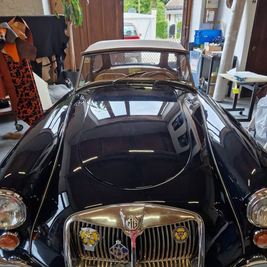 MG MGA noire classique, calandre chromée avec badges et toit beige décapotable dans un garage.