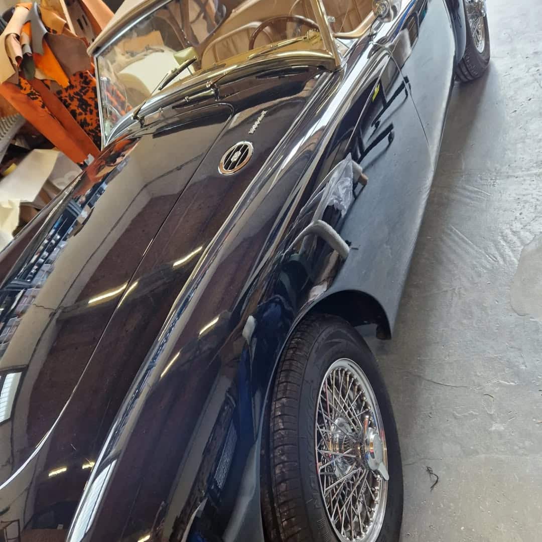 Austin-Healey de collection bleu foncé avec jantes à rayons chromées dans un atelier de restauration automobile.