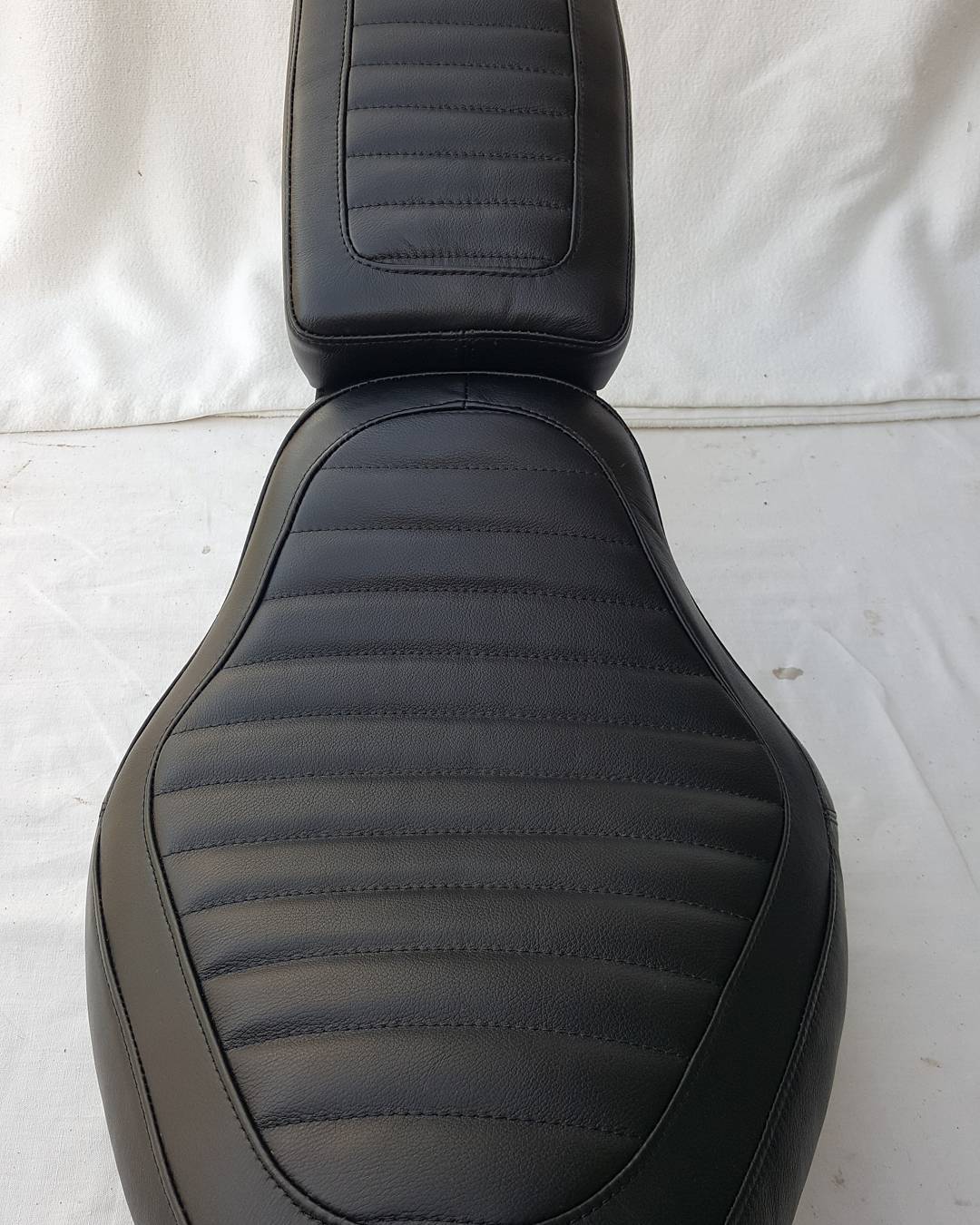 Selle de moto en cuir noir avec surpiqûres horizontales style tuck and roll sur fond blanc.