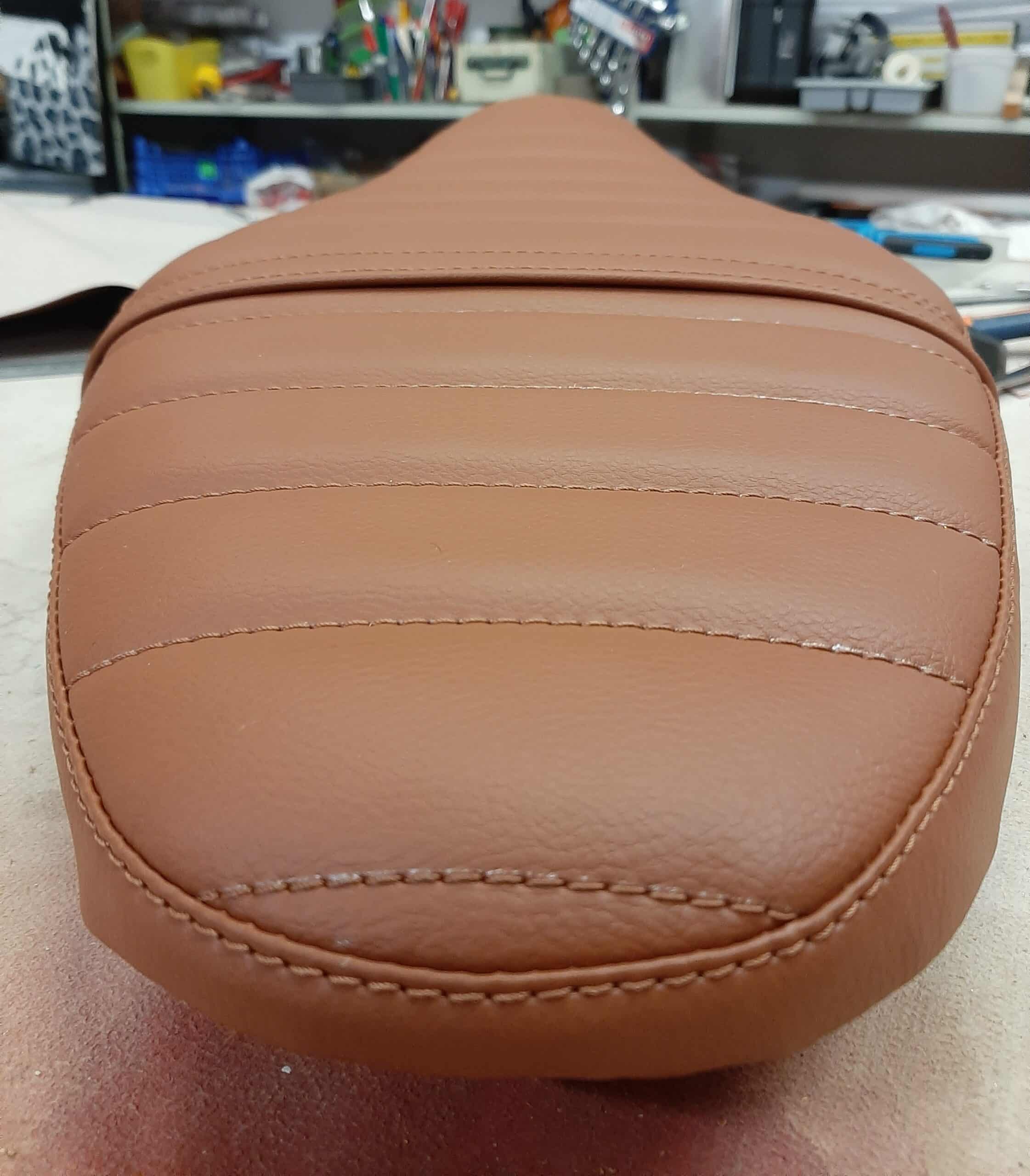 Selle de moto en simili cuir marron avec surpiqûres horizontales et coutures apparentes style vintage.