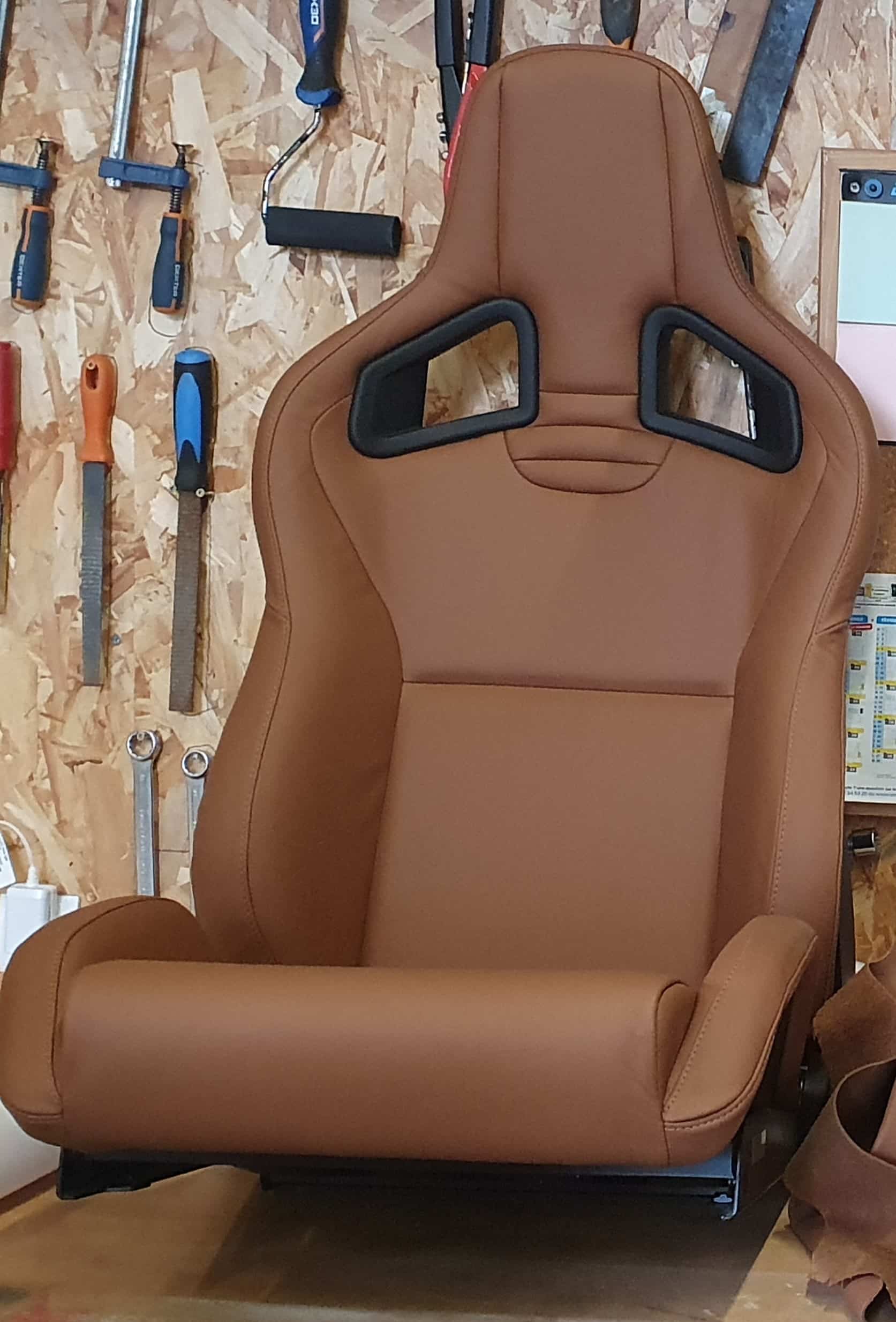 Siège baquet en cuir marron de style course dans un atelier de mécanique avec des outils en arrière-plan.