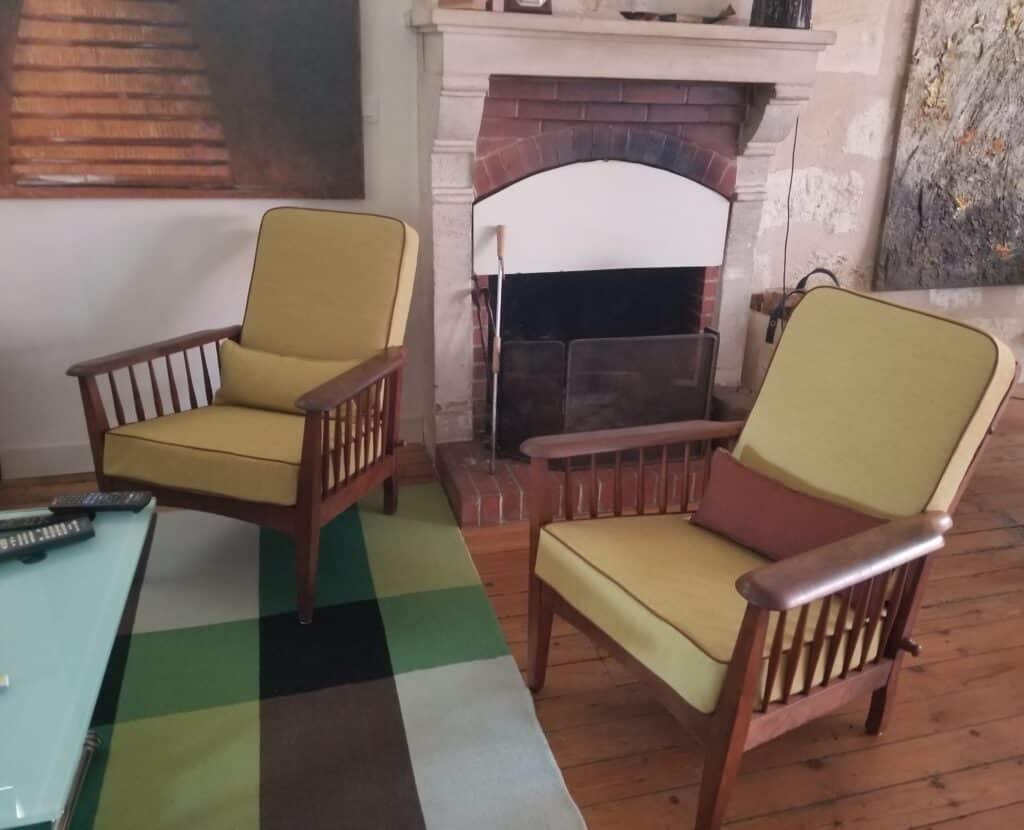 Deux fauteuils vintage jaunes en bois, tapis géométrique vert et cheminée classique dans un salon chaleureux.