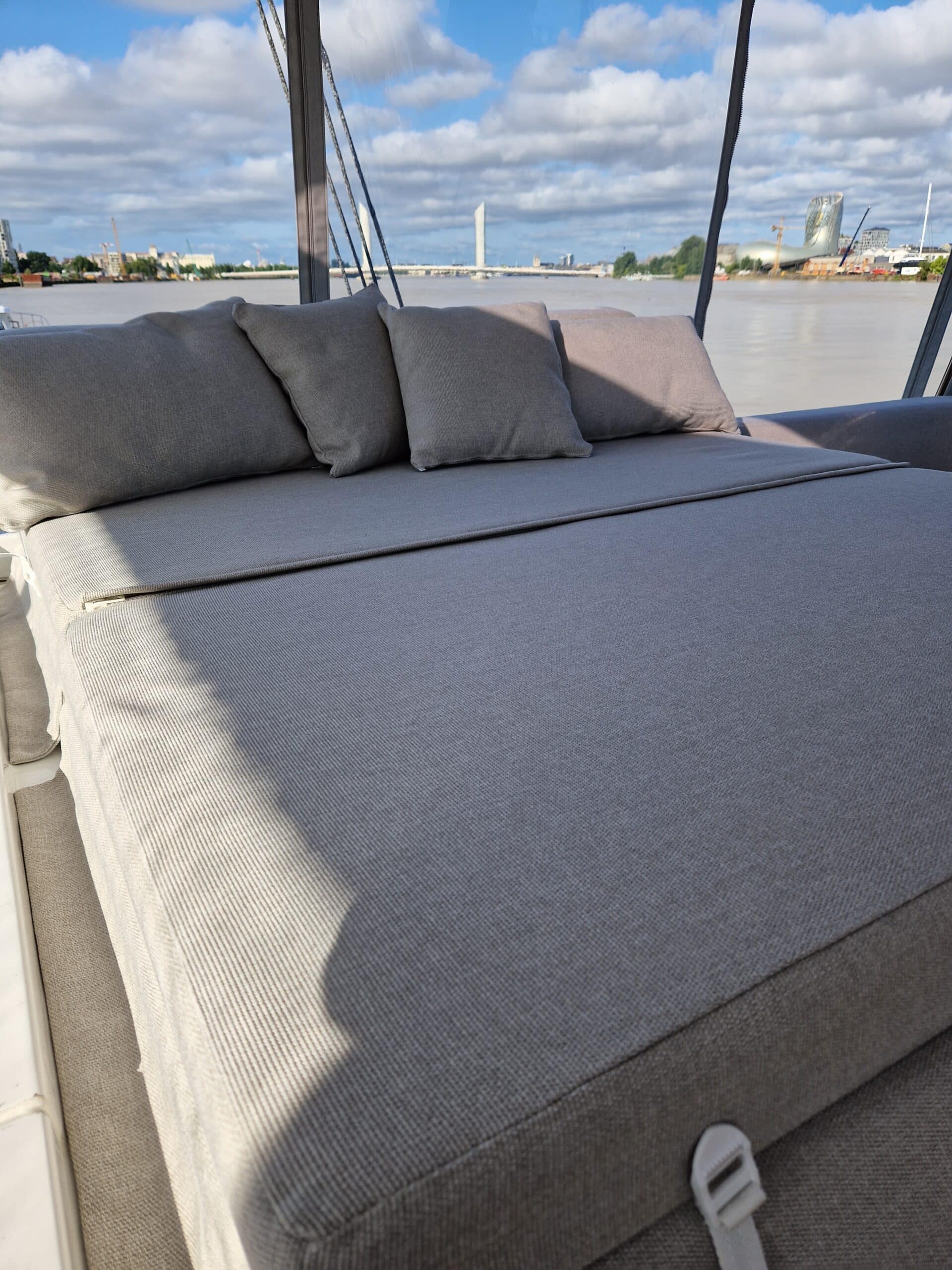 Bain de soleil gris sur pont de bateau, coussins assortis, vue sur Garonne et Cité du Vin à Bordeaux.