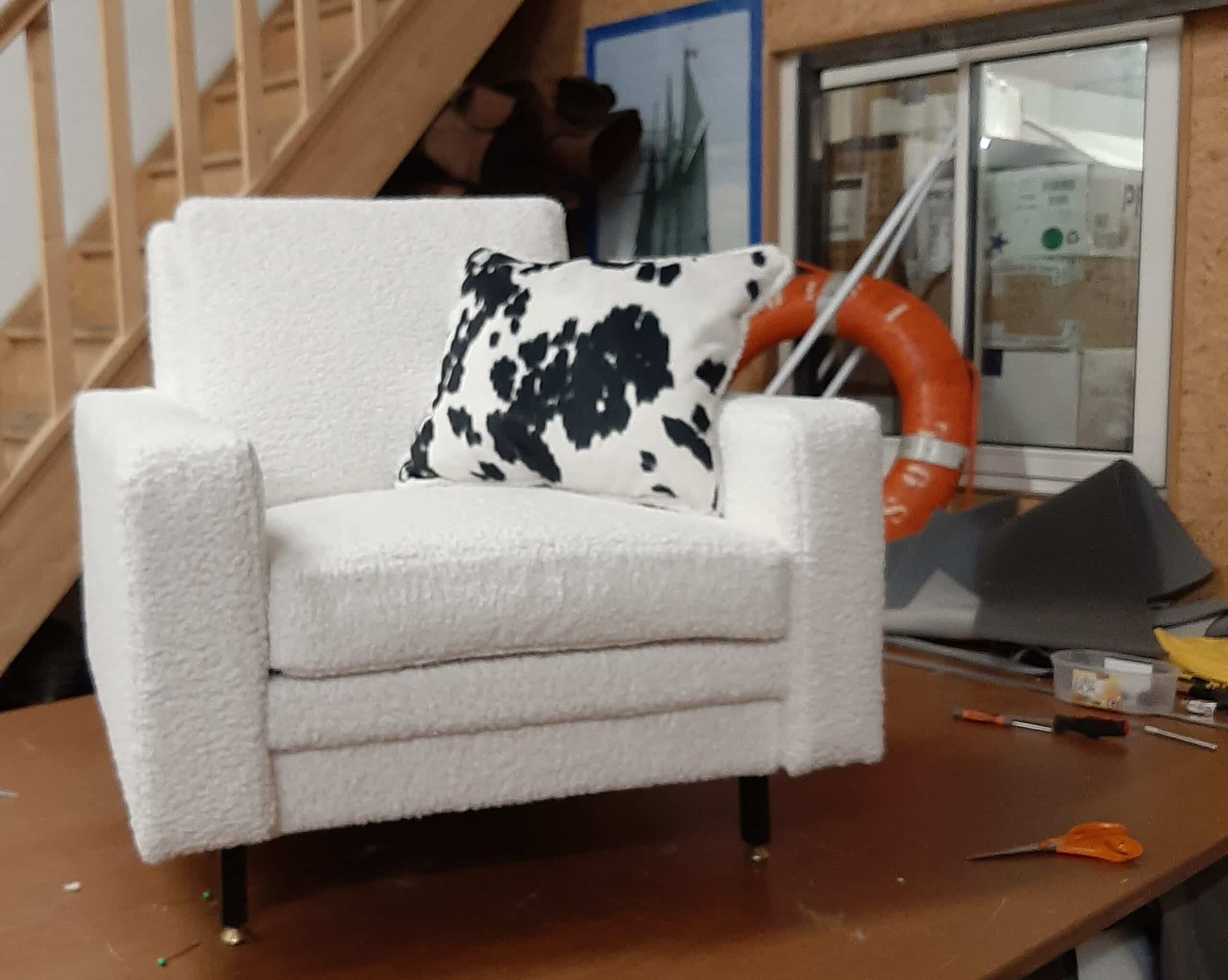 Fauteuil en bouclé blanc, coussin motif vache noir et blanc, design moderne et confortable dans un atelier.