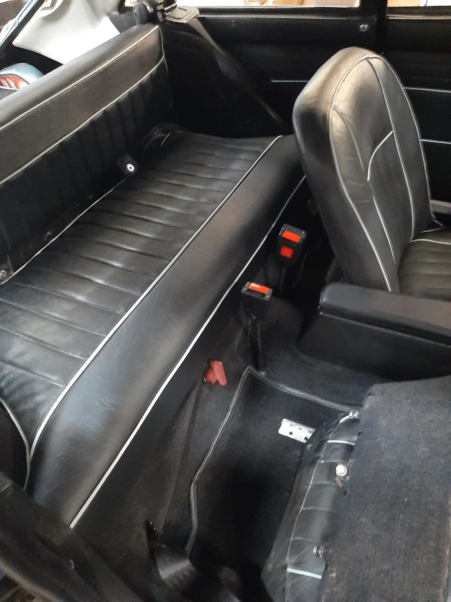 Sièges arrière en cuir noir à liseré blanc d'une voiture ancienne avec interrupteur de sécurité rouge sur le plancher.