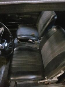 Intérieur de voiture vintage avec sièges en vinyle noir, volant classique et levier de vitesses manuel.