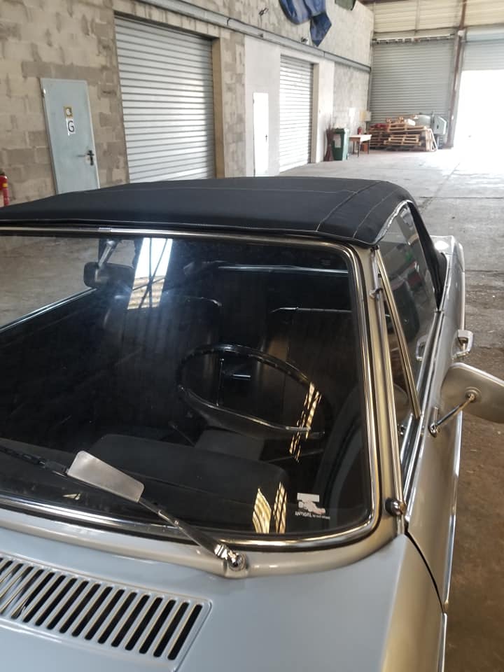 Mercedes-Benz SL décapotable argentée avec toit souple noir dans un garage. Intérieur vintage visible.