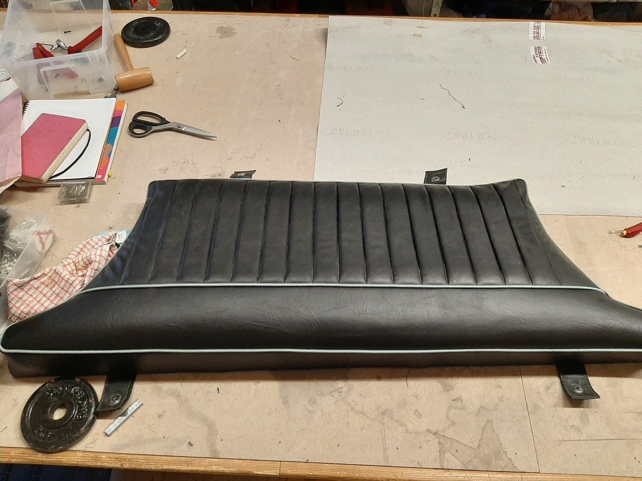 Siège auto en similicuir noir avec plis verticaux sur un établi de sellerie avec outils de travail.