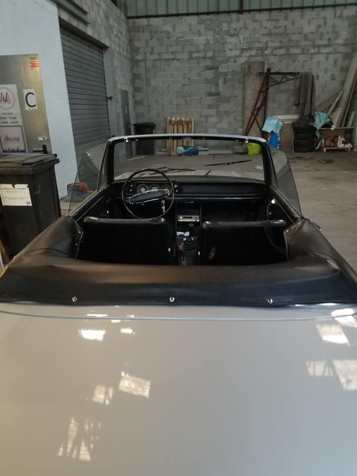 Intérieur d'une voiture décapotable vintage grise avec sièges en cuir noir, vue de l'arrière dans un garage rustique.